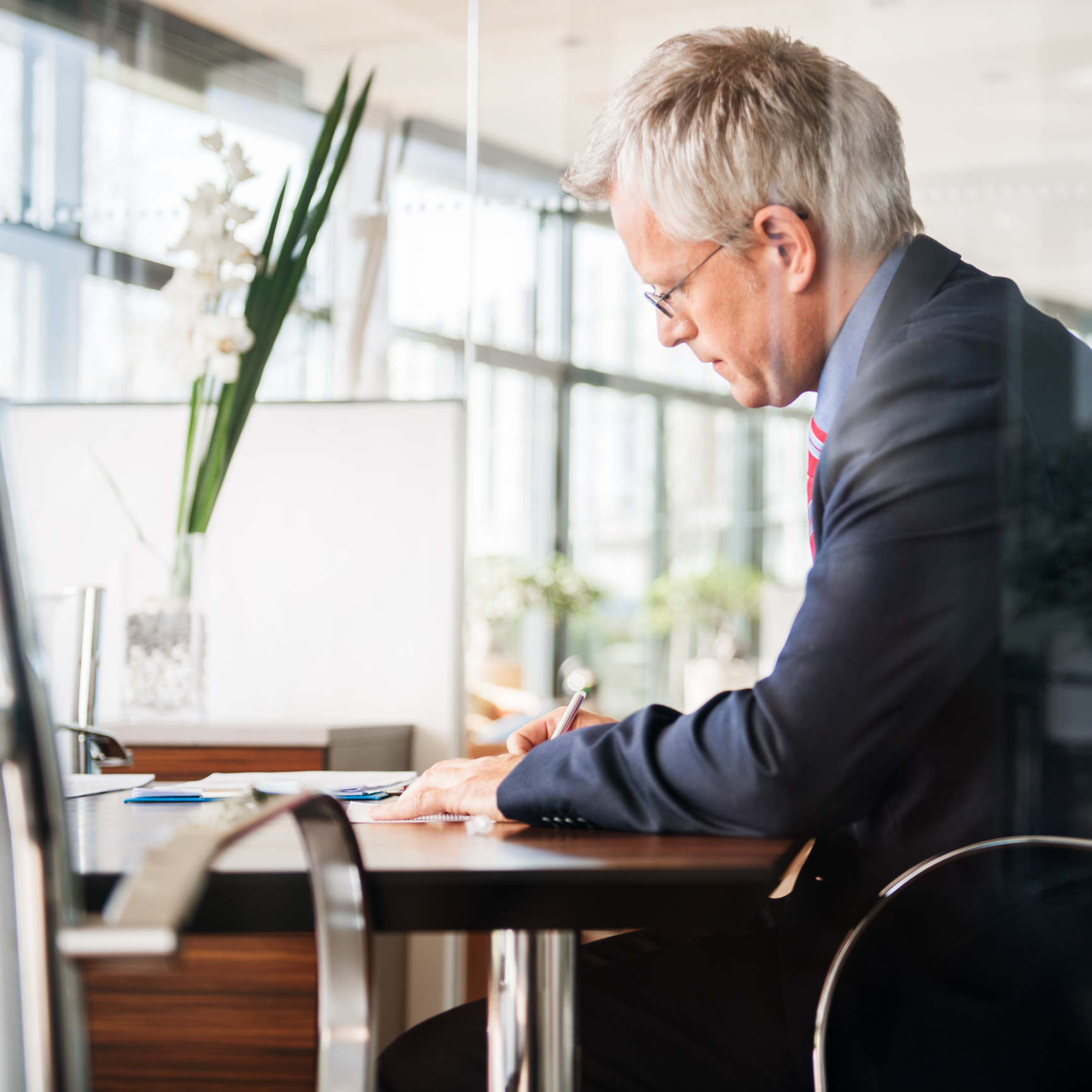 Mature businessman signing a paper or contract on a desk. Side view.